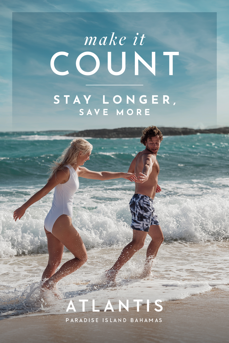 Make It Count: Stay Longer, Save More at Atlantis Bahamas. | A smiling couple holding hands and running through the ocean waves on a sunny beach.