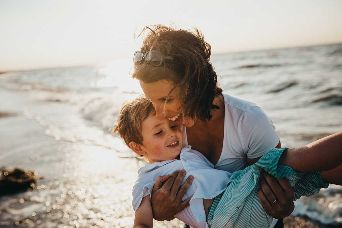 Woman holding son on a beach.