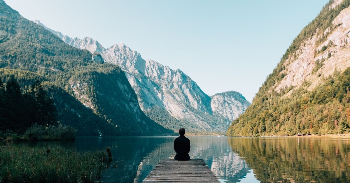 A person at the end of a dock on a lake in a mountain ravine staring into the horizon.looking