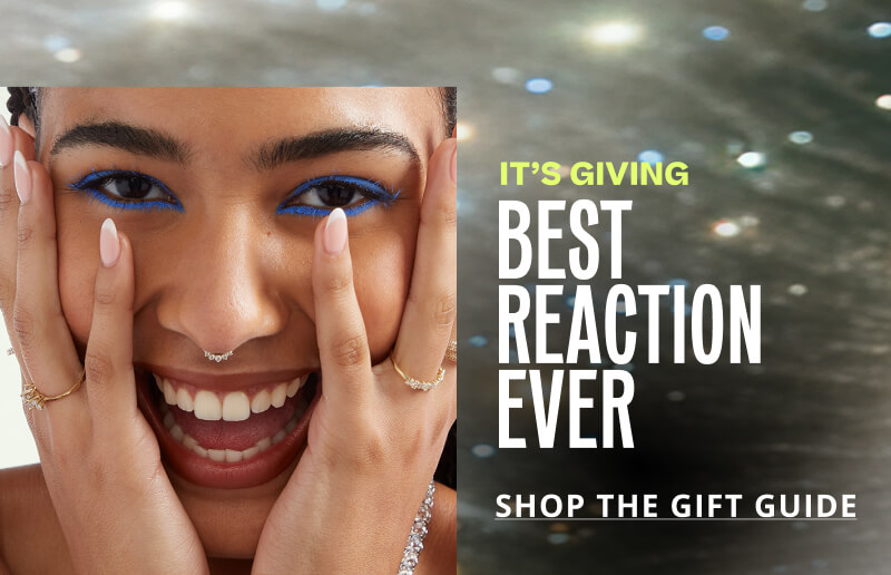 Model smiling, wearing jewelry. Giving: best reaction ever. Click here to shop the gift guide