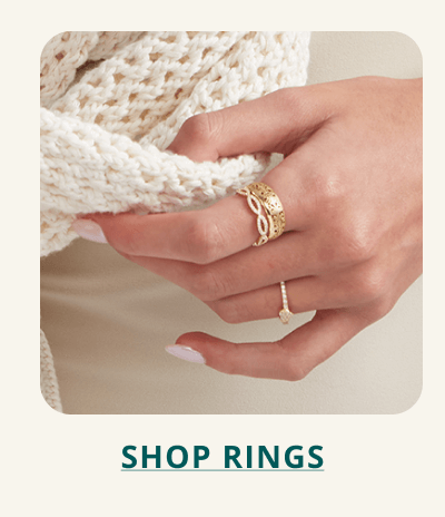 Focus on hand with stacked dainty, uniquely patterned gold rings. Click here to shop rings