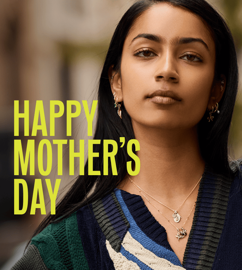 Model layered in gold dangling huggies & gold necklaces with multiple charms. Happy Mother’s Day.