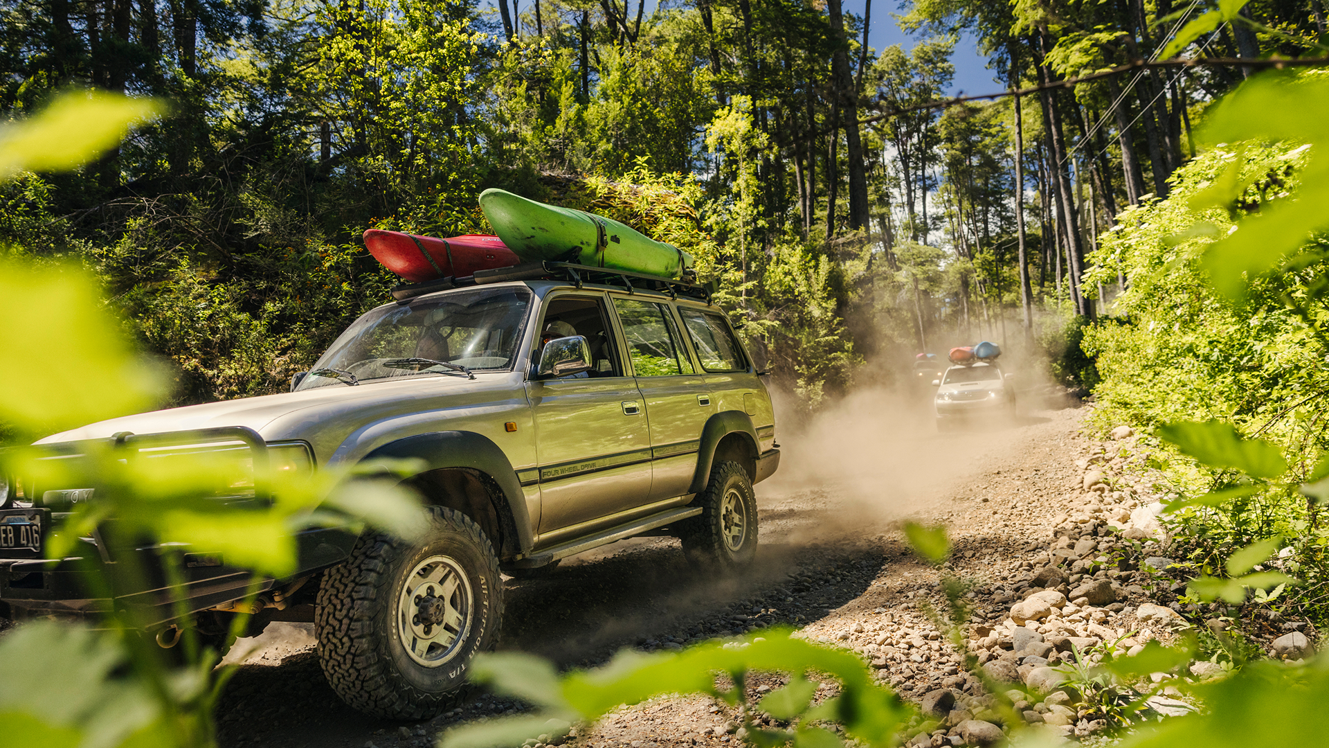 vehicle with kayaks on roof driving down dirt road surrounded by trees