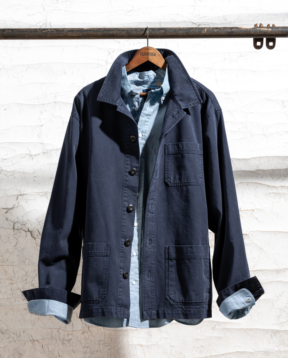 A Bills Khaki  navy Over Shirt and Bills Khaki Standard Shirt hang from a hangar amonst an industrial setting