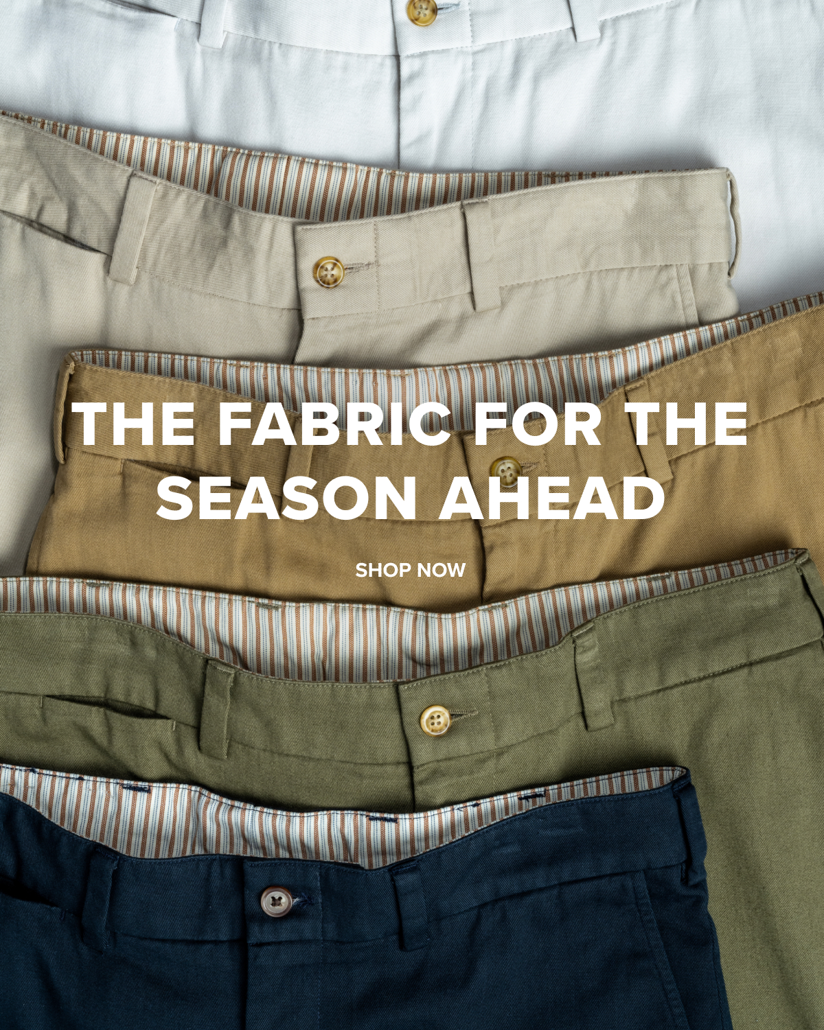 Navy, Olive, British Khaki, Khaki, and Stone colored Bills Khaki Vintage Twill Khakis sit arrayd on a flat surface. The crop shows the belt, button and zipper area of each. Text reads 