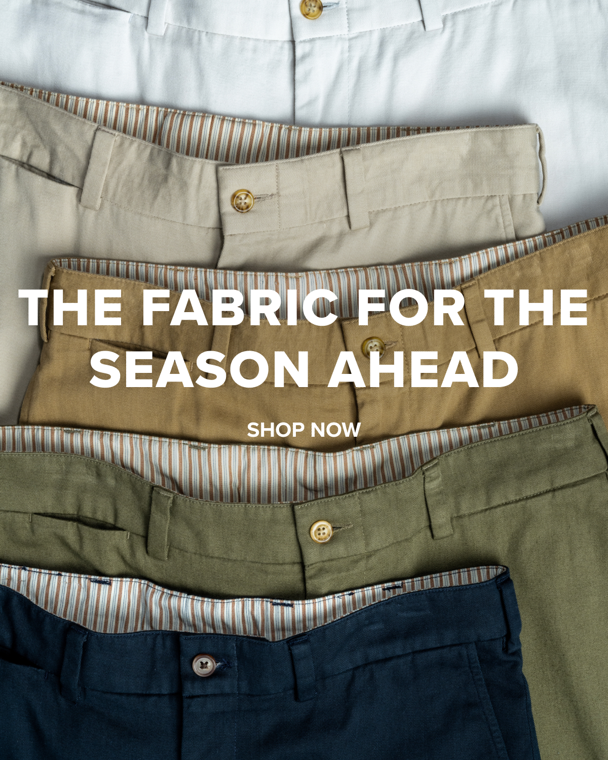 Navy, Olive, British Khaki, Khaki, and Stone colored Bills Khaki Vintage Twill Khakis sit arrayd on a flat surface. The crop shows the belt, button and zipper area of each. Text reads 