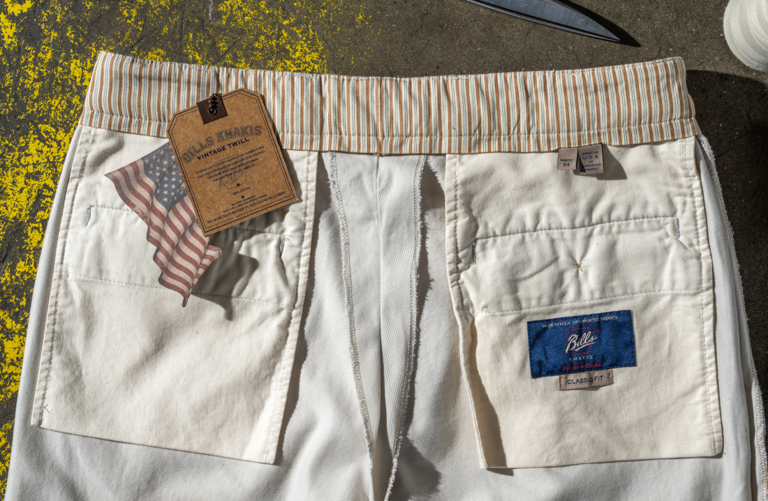 A pair of Bills Khaki Vintage Twill paints sits inside out showing the seam and quality work of the pockets, belt and zipper area. The tag is displayed along with an American Flag 