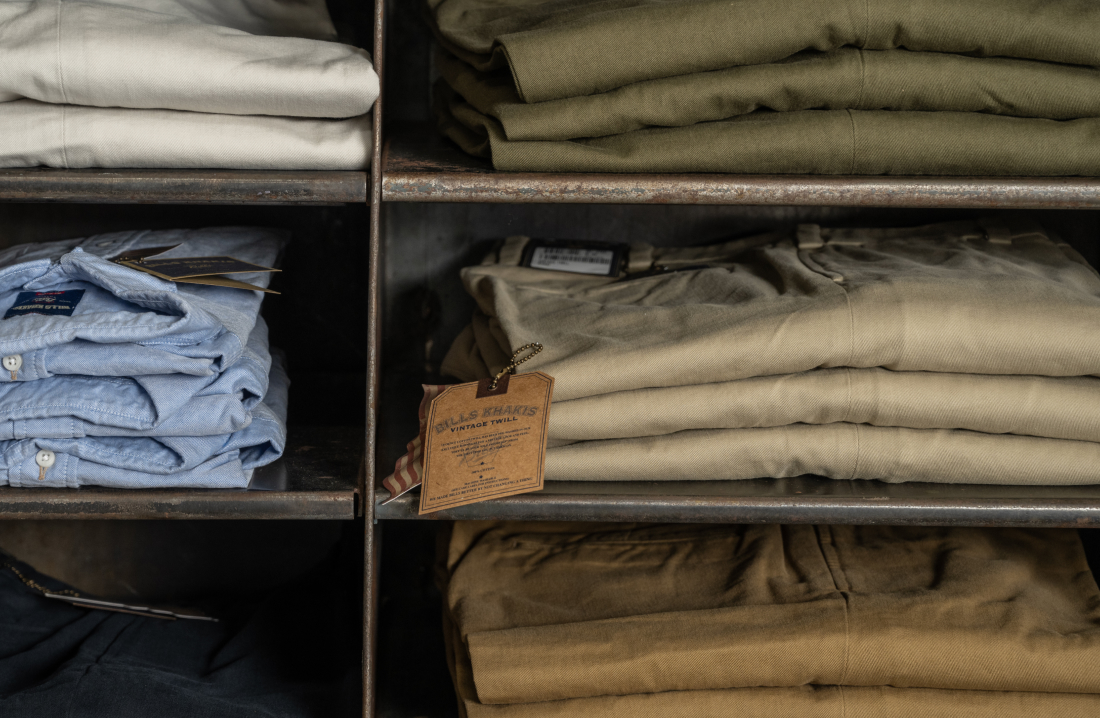 Multiple pairs of Bills Khaki Vintage Twill pants sit folded in a metal shelf