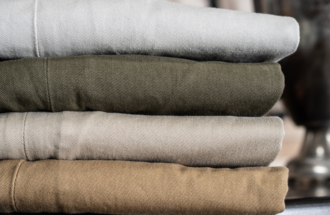 Multiple pairs of Bills Khaki Vintage Twill pants are stacked folded. The photo crops in and shows a corner of the stack to show the fabric detail and quality