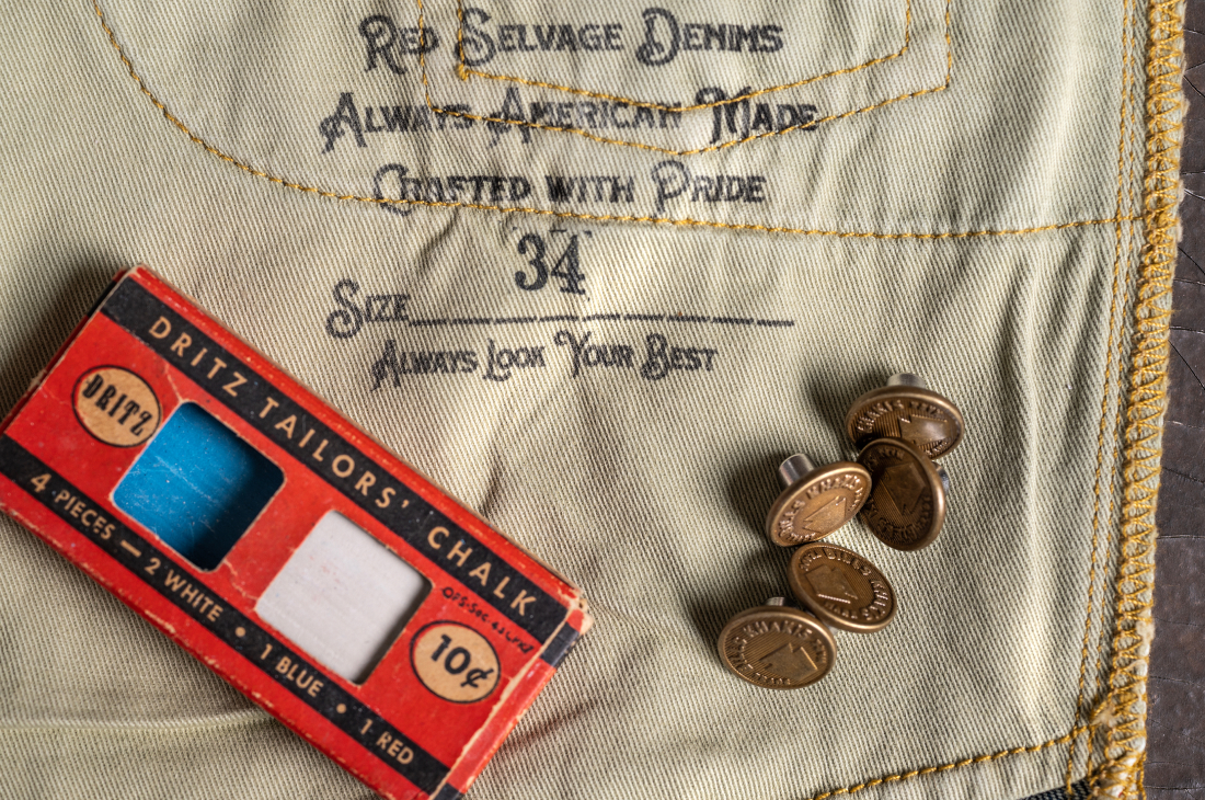 A close up on loose bronze buttons and the inner pocket + sitching of a pair of Gene Montesano x Bills Khakis Red Selvage Denim collaboration pants
