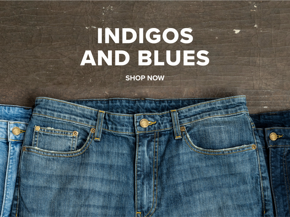 Three pairs of Bills Khakis Denim pants in three tones of blue lay on a brown industrial surface. Text Reads: Indigos and Blues | Shop Now