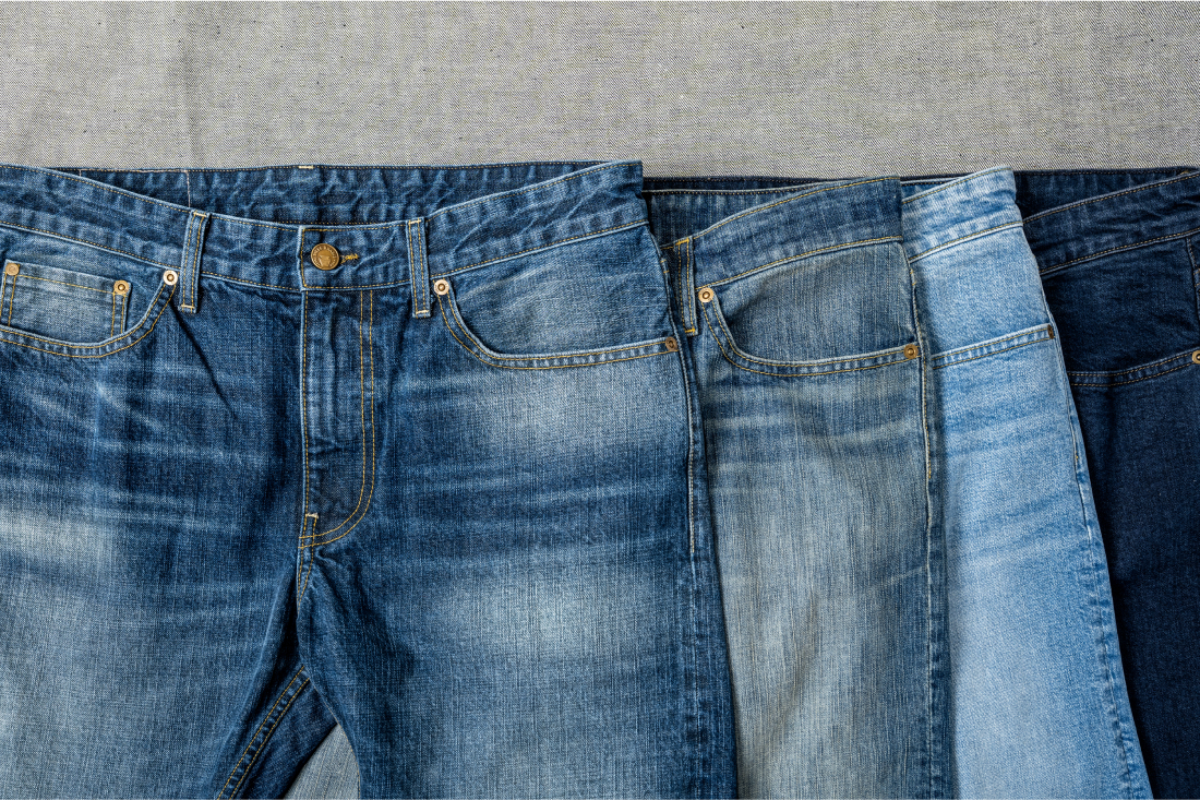 Another aray of Bills Khakis denim pants lay flat in four colorways/washes on a gray backdrop