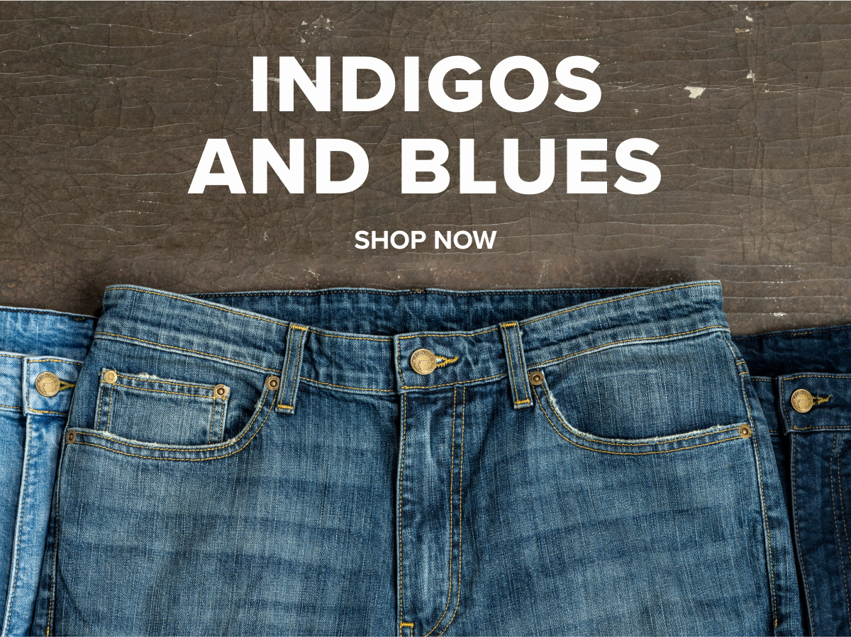 Three pairs of Bills Khakis Denim pants in three tones of blue lay on a brown industrial surface. Text Reads: Indigos and Blues | Shop Now