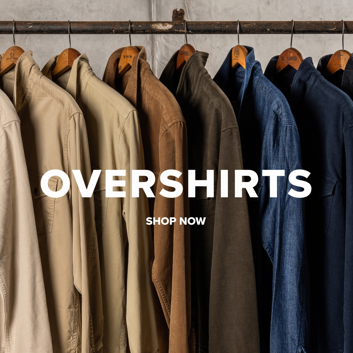 An array of Bills khaki overshirts from light khaki to brown to dark navy and black hang from an industrial pole and hangers. Text reads: Overshirts | Shop Now