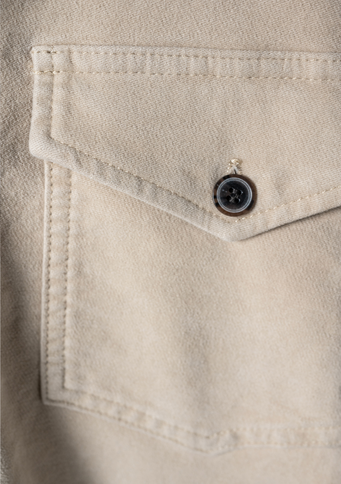 A close up of a stone colored Bills Khaki chore jacket pocket stitching and button