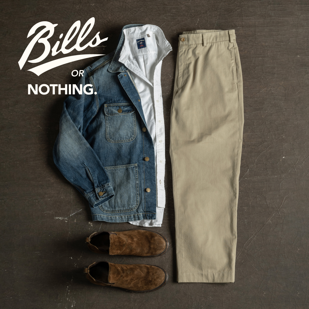 A pair of Bills Khakis Original Twill pants, Bills Khaki Denim Jacket, and Bills Khaki Oxford Shirt lay on a brown industrial surface with brown suede shoes. A logo reads Bills or Nothing