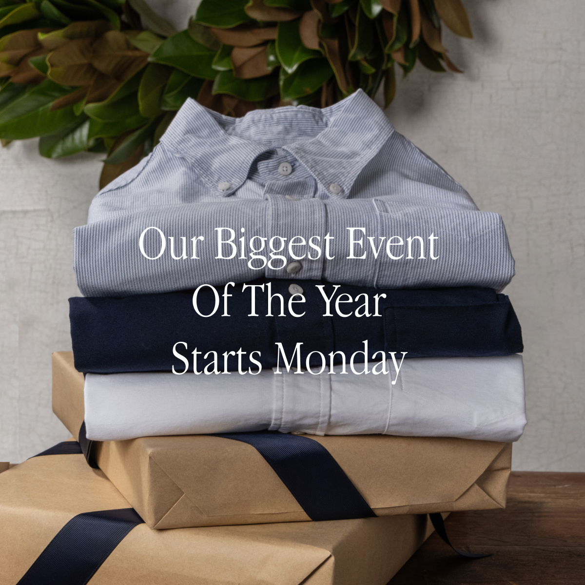A stack of Bills Khaki Oxford Shirts sit folded ontop of two gift wrapped boxes with a wreath on the wall in the background. Text reads 'Our Biggest Event of the Year Starts Monday'