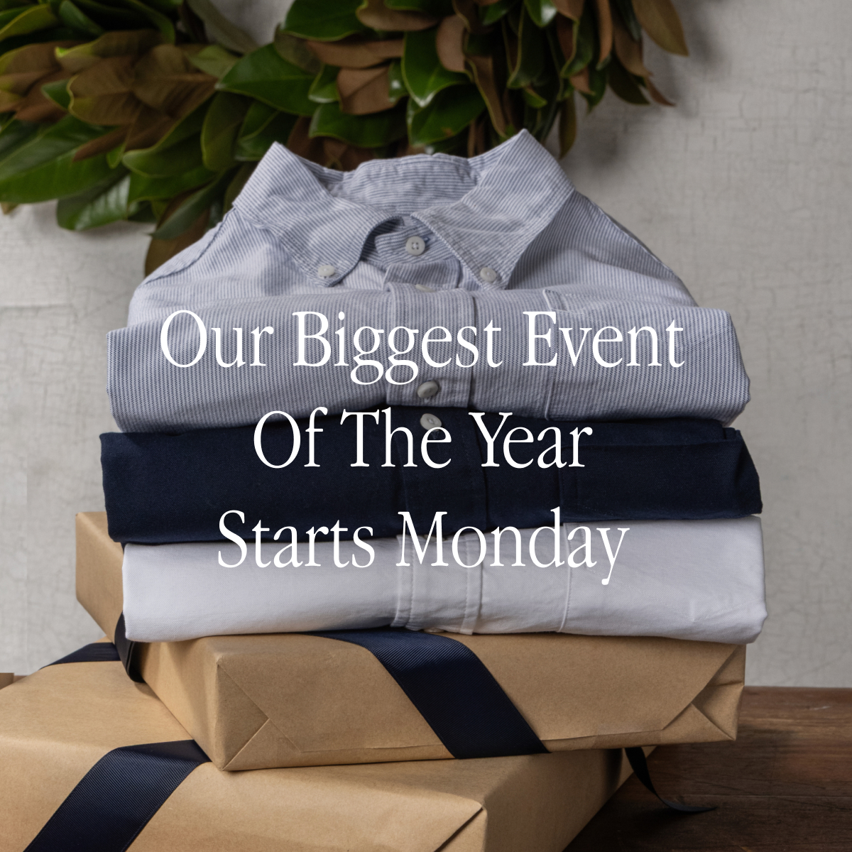 A stack of Bills Khaki Oxford Shirts sit folded ontop of two gift wrapped boxes with a wreath on the wall in the background. Text reads 'Our Biggest Event of the Year Starts Monday'