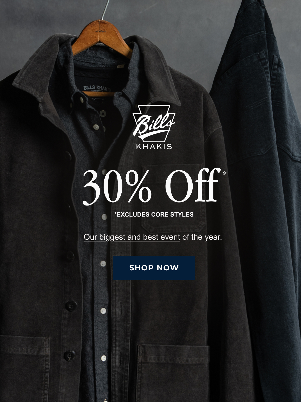 A black Bills Khaki Chore Jacket and charchoal Standard fit shirt hang against an industrial grey background alongside a pair of hanging navy Bills Khaki pants. The Bills Khaki logo overlays the image along with text that reads: 30% Off* | *Excludes Core styles | Our biggest and best event of the year | Shop Now
