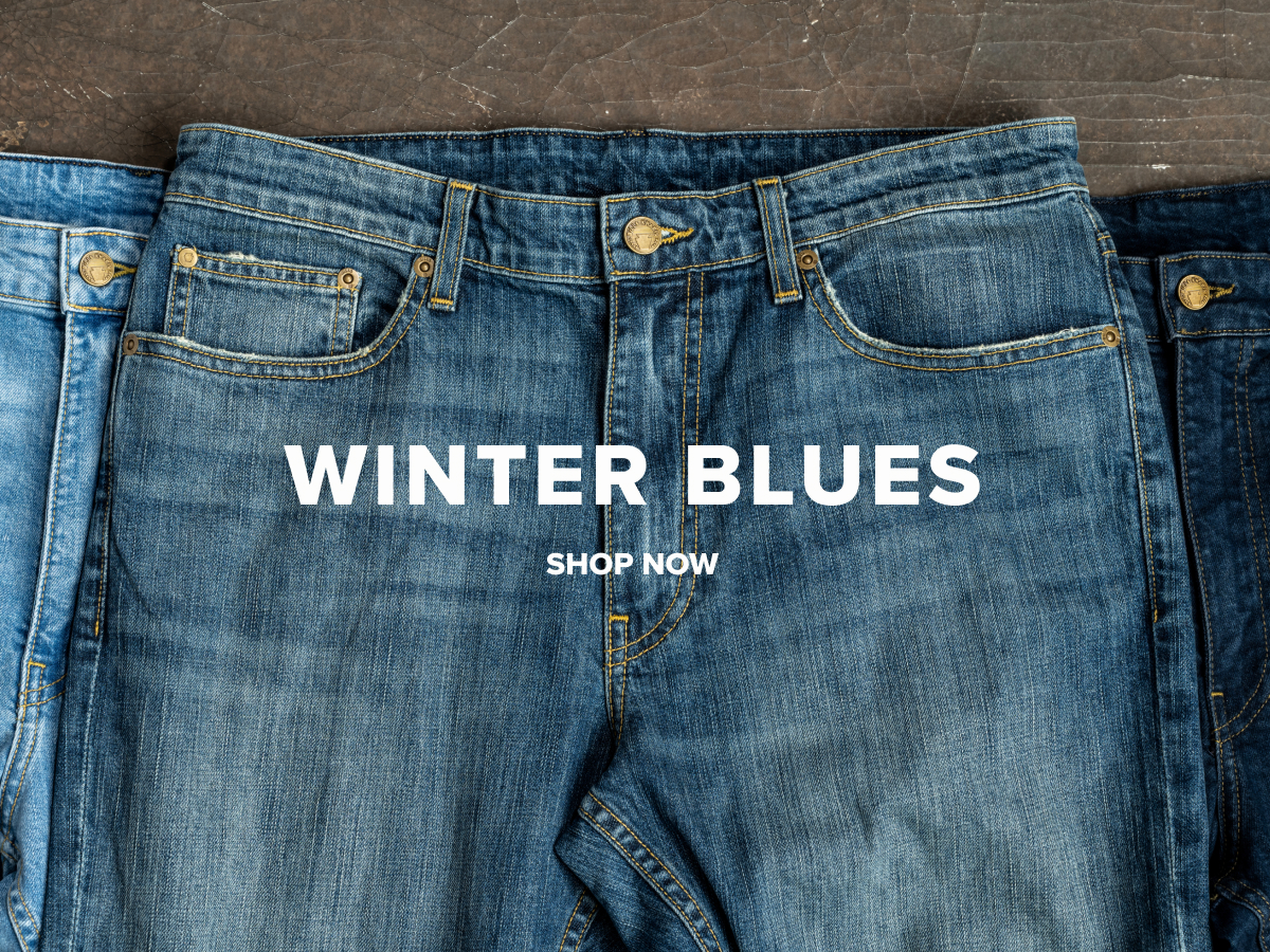 Pairs of different tones of blue Bills Denim lay on an industrial grey surface. Text reads: Winter Blues | Shop Now