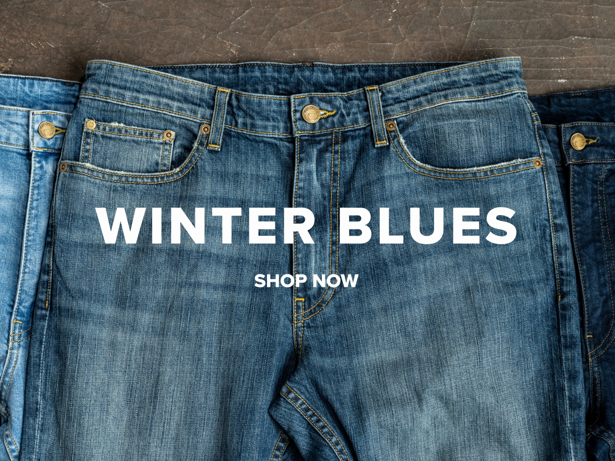 Pairs of different tones of blue Bills Denim lay on an industrial grey surface. Text reads: Winter Blues | Shop Now