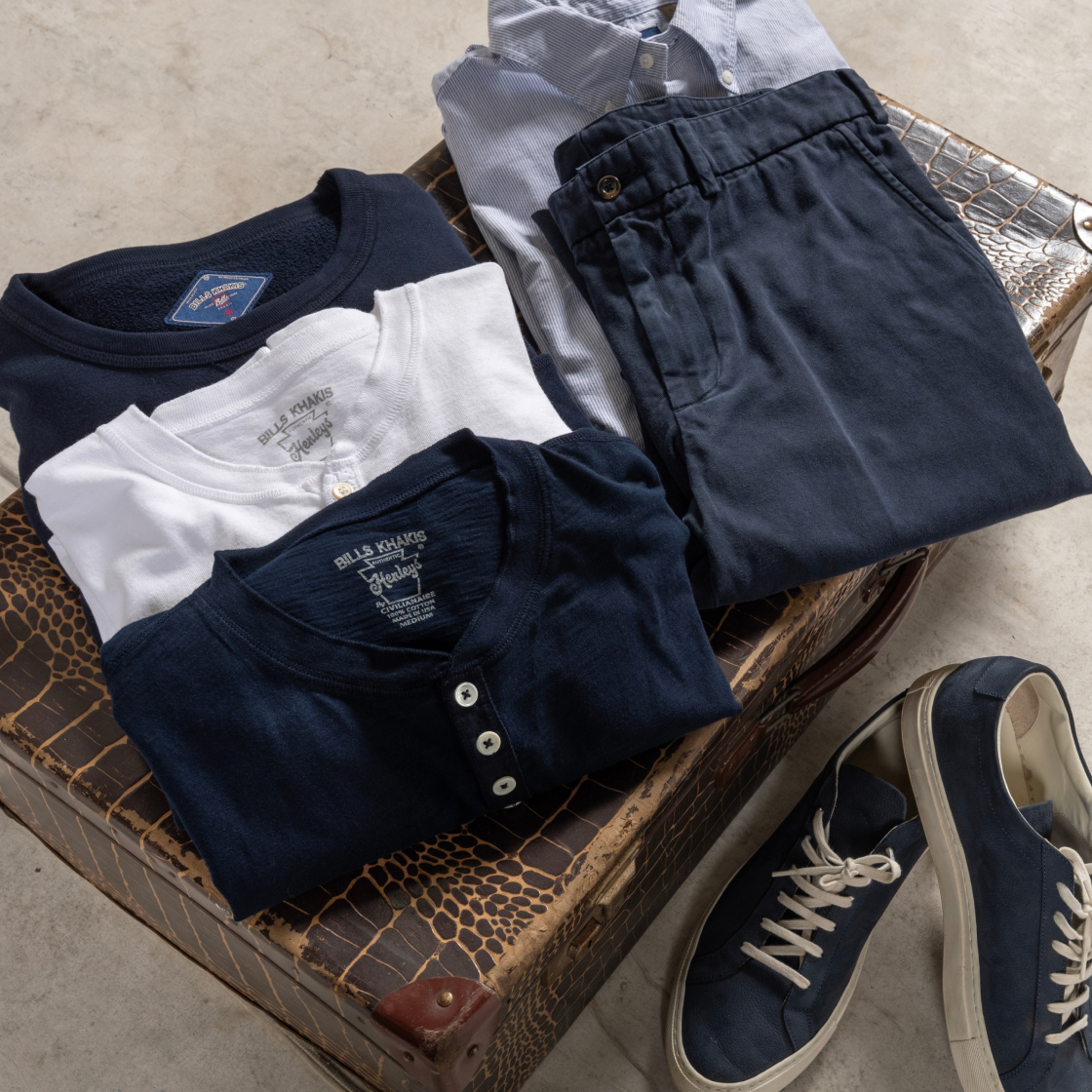 Different blue, light blue and white Bills Khaki clothing pieces sit folded on display on vintage suitcase