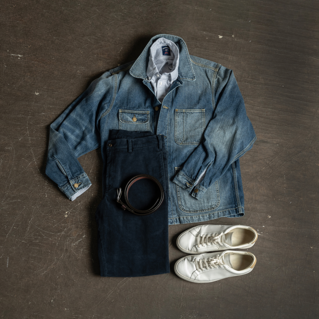 A full outfit highlighted by a Bills Khaki denim jacket and navy pants sit displayed flat on an indutrial surface