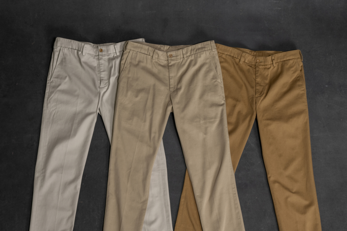 Three pairs of Bills Khakis khaki pants lay on display on an industiral stone surface