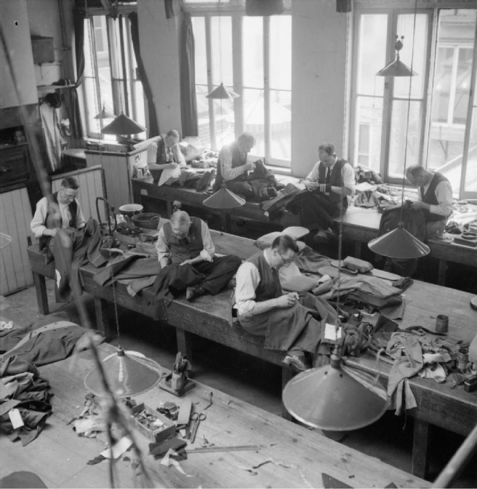 A photo of men in the early-mid 1900's at long tables stiching textiles
