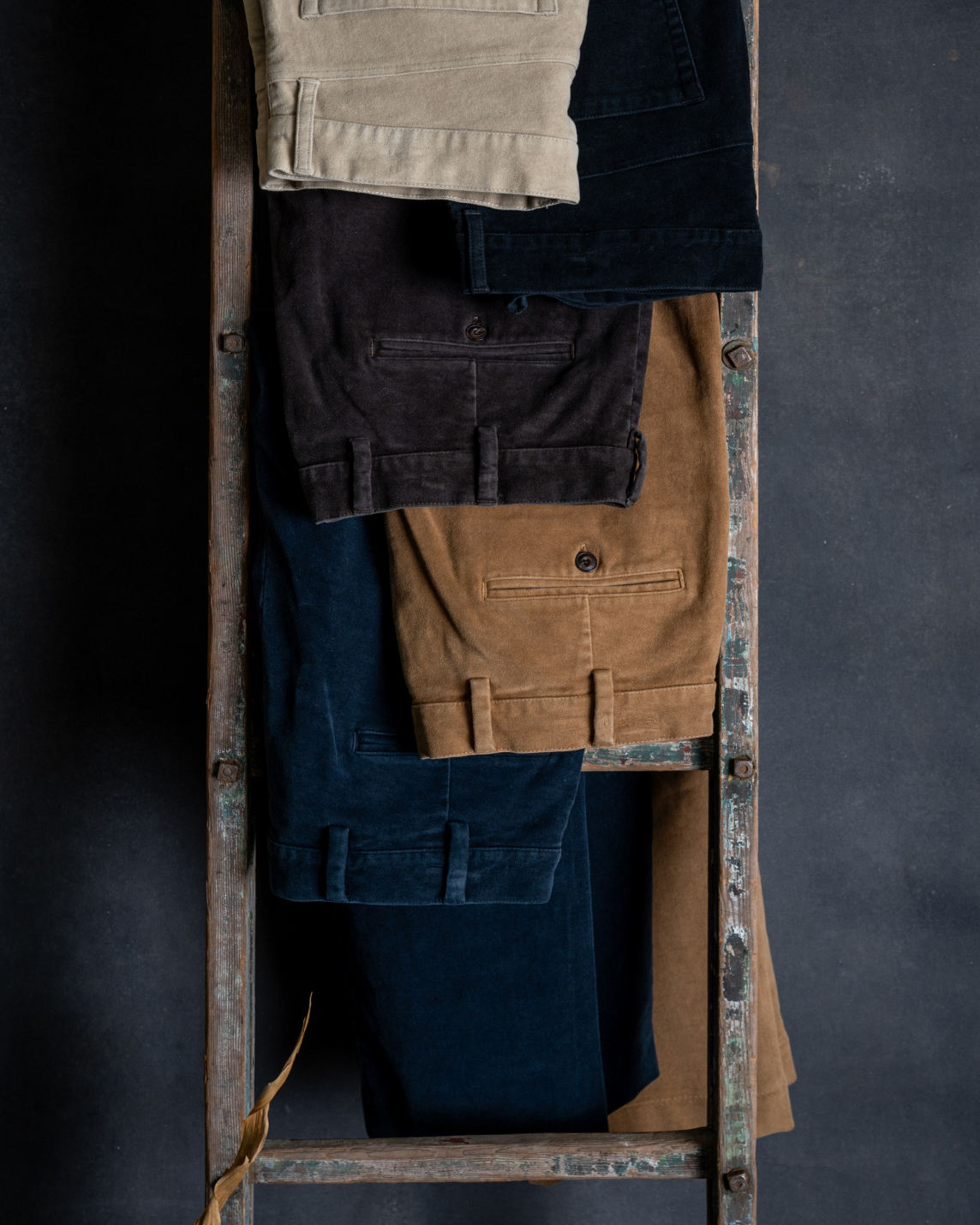 Five pairs of Bills Khakis moleskin pants hang from an industrial ladder