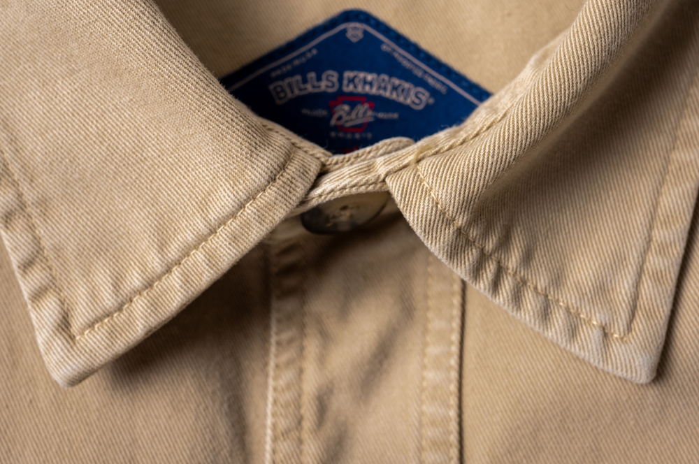 A close up detail of the collar, top button, and tag of a desert tan heritage wash chore jacket