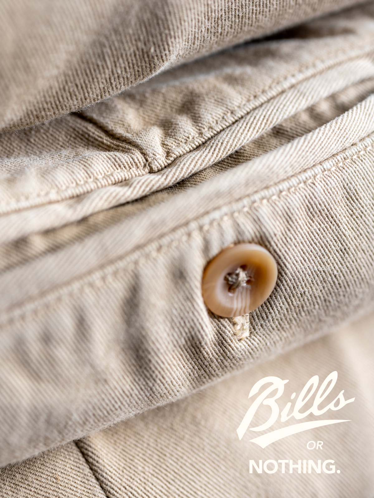A close up of the back pocket button area of Bills Khakis Original Twill pants. A logo reads Bills Or Nothing.