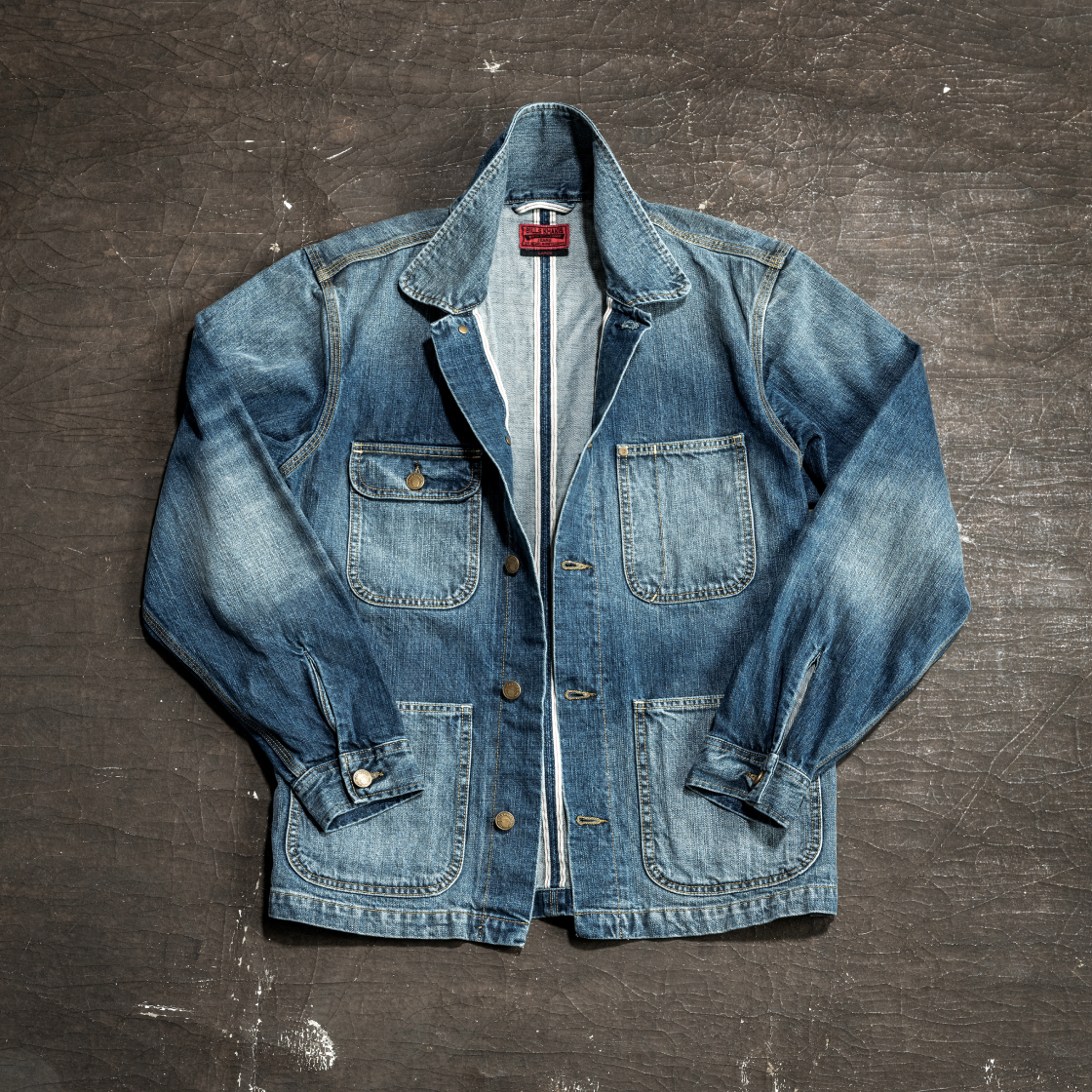 A Bills Khakis red selvage denim jacket lays face up on an dark industrial service