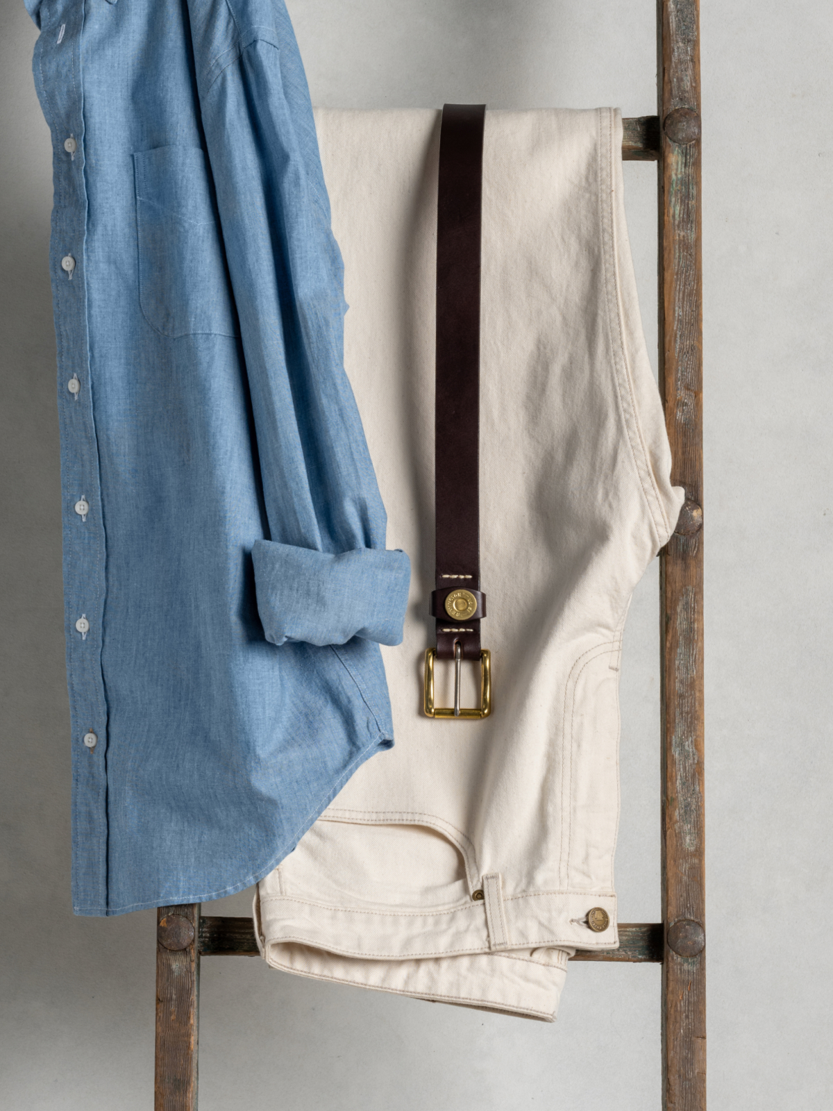 Bills Khakis Bullard Twill in bone hanging from a ladder with a Bills belt and blue standard fit shirt