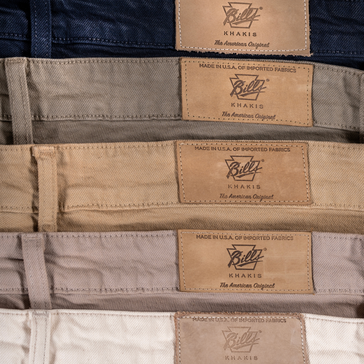 A array of colors of Bills Khaki 5 pocket bullard twill pants showing the belt and back tag detail
