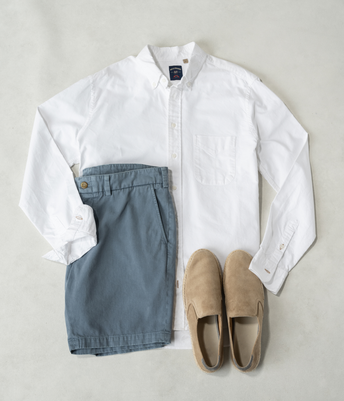 A white Bills Khakis Gitman shirting laying on a warm surface with Bills shorts and a pair of slip on loafers