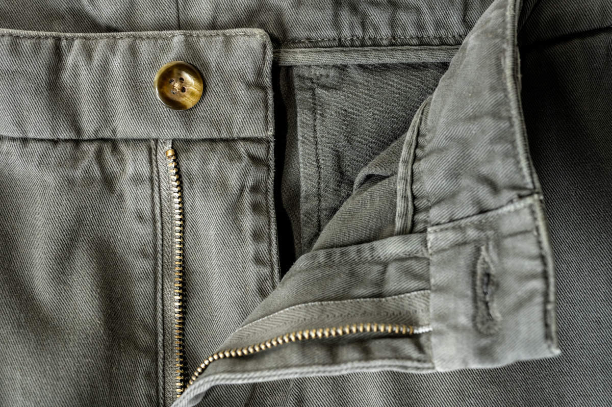 A closeup of the open button and zipper of Bills Khakis shorts in olive