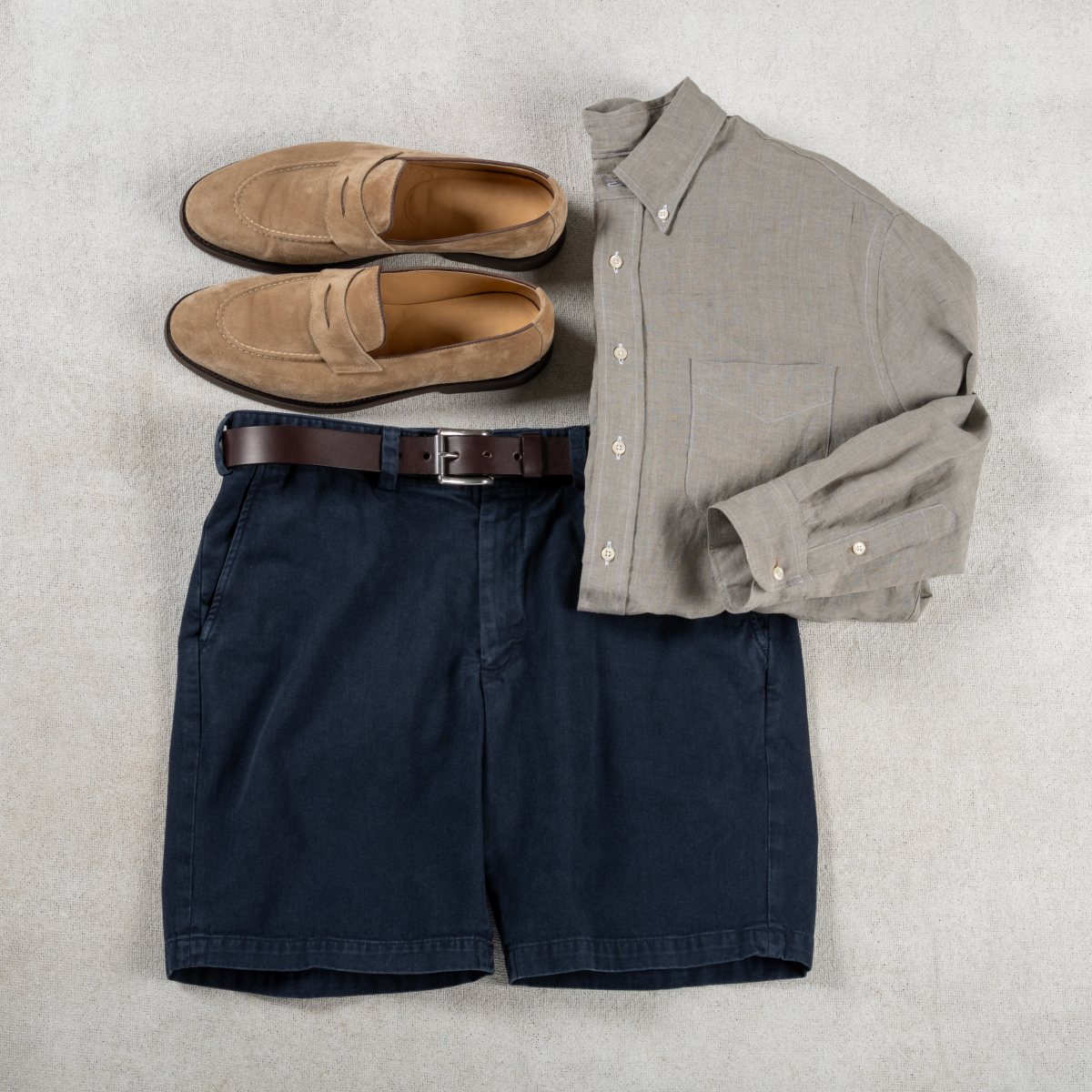 A pair of navy Bills Khakis Heritage Wash shorts sit with a grey Bills Standard fit shirt and loafers