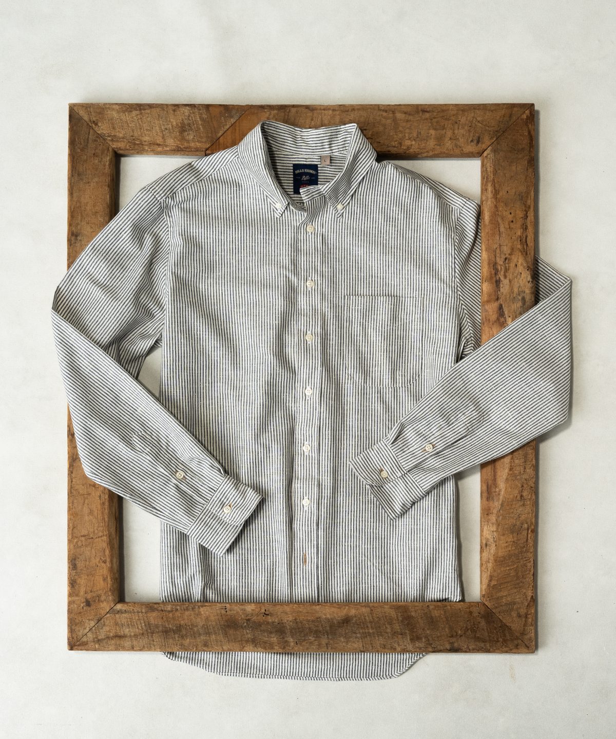 A Natural Cotton Bills Khakis standard fit shirt lays flat intwined with a vintage wood picture frame on a light colored surface