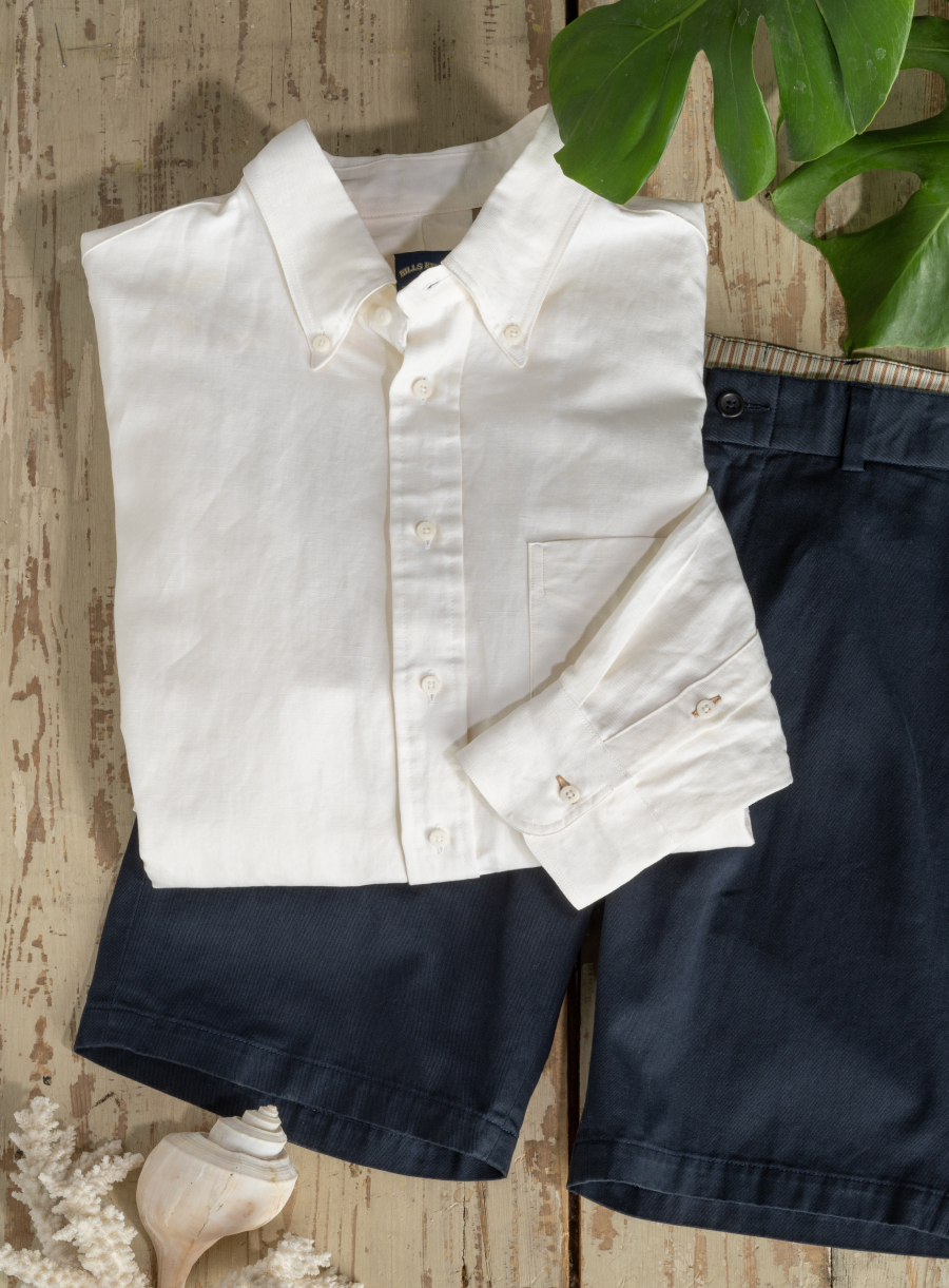 A natural cotton shirt and Bills Khakis shorts lay on a wooden surface surrounded by some beach objects