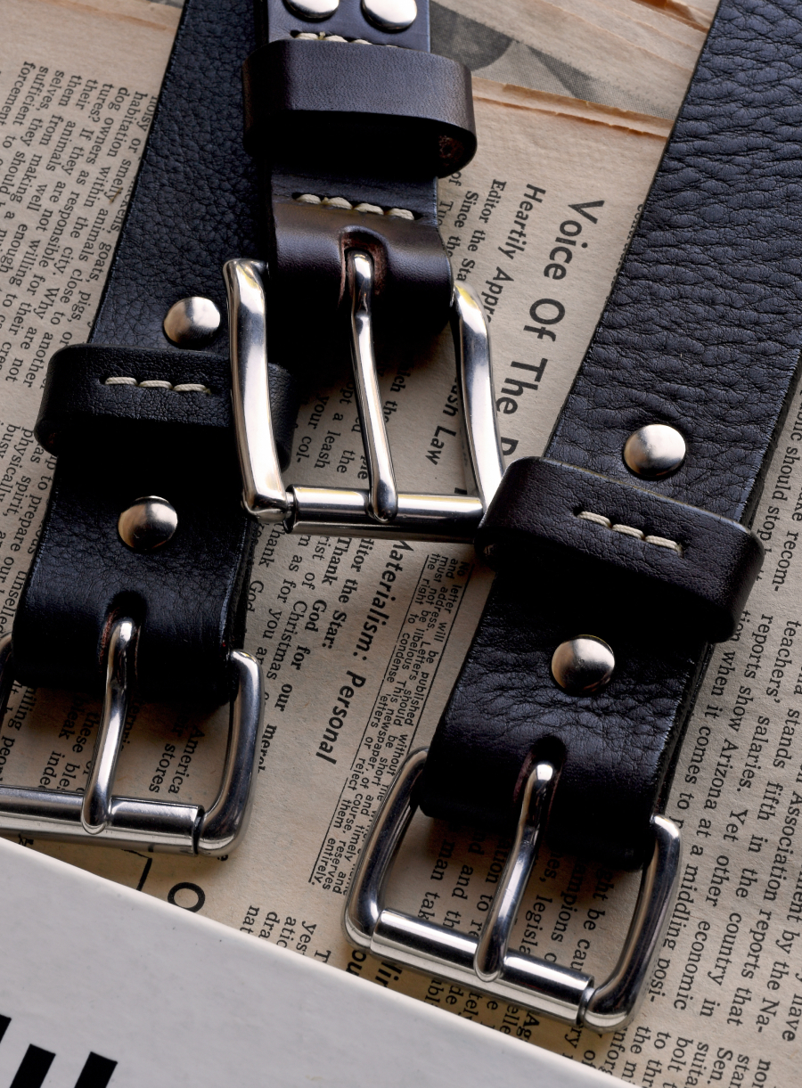Three Bills Khakis belts lay along vintage newspapers