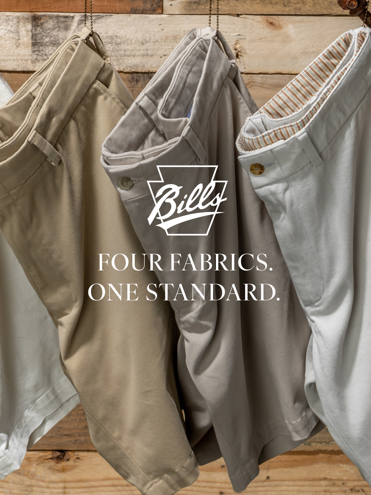 Four Bills Khakis Vintage Twill Shorts hang against a wooden pallet backdrop. Overlay text reads 'Four Fabircs. One Standad.' alongside the Bills Khakis logo