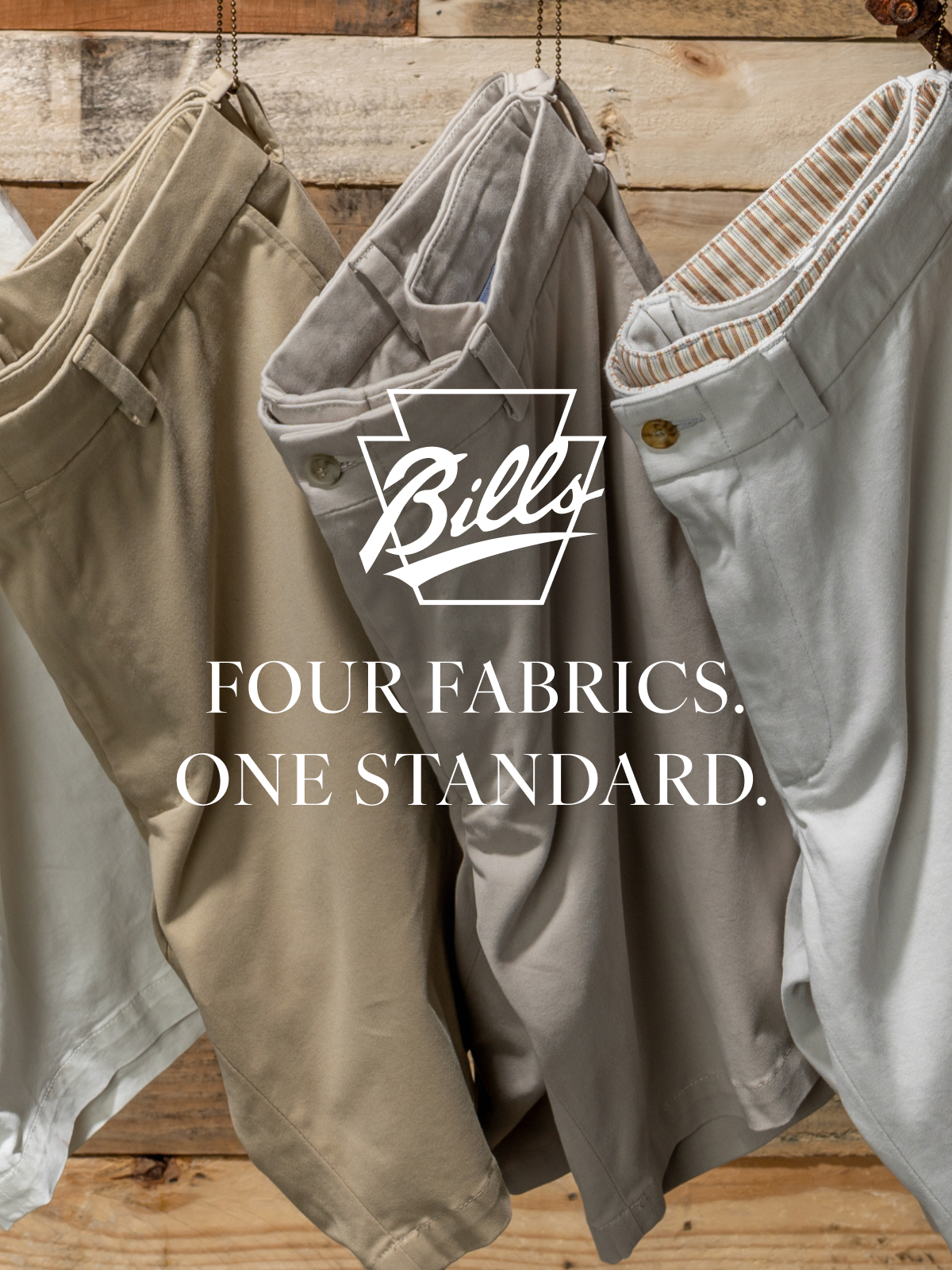 Four Bills Khakis Vintage Twill Shorts hang against a wooden pallet backdrop. Overlay text reads 'Four Fabircs. One Standad.' alongside the Bills Khakis logo