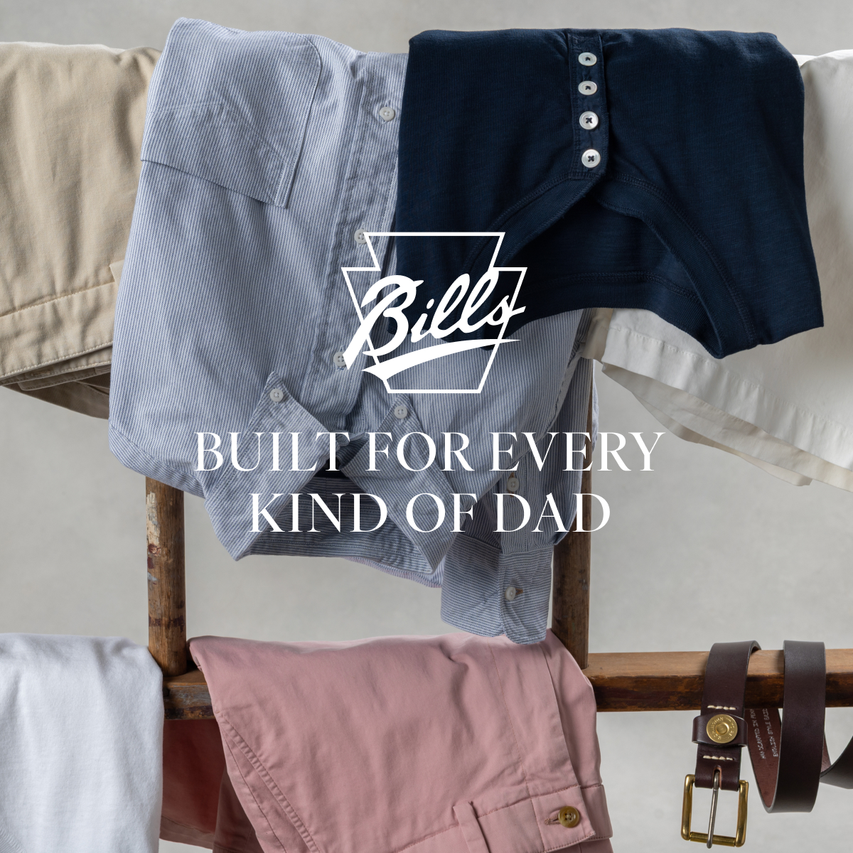 Bills Khakis shirts, shorts, henleys and belts lay relaxed on wooden polls. Text overlay has the Bills Khakis logo along with text 'Built for Every Kind of Dad'