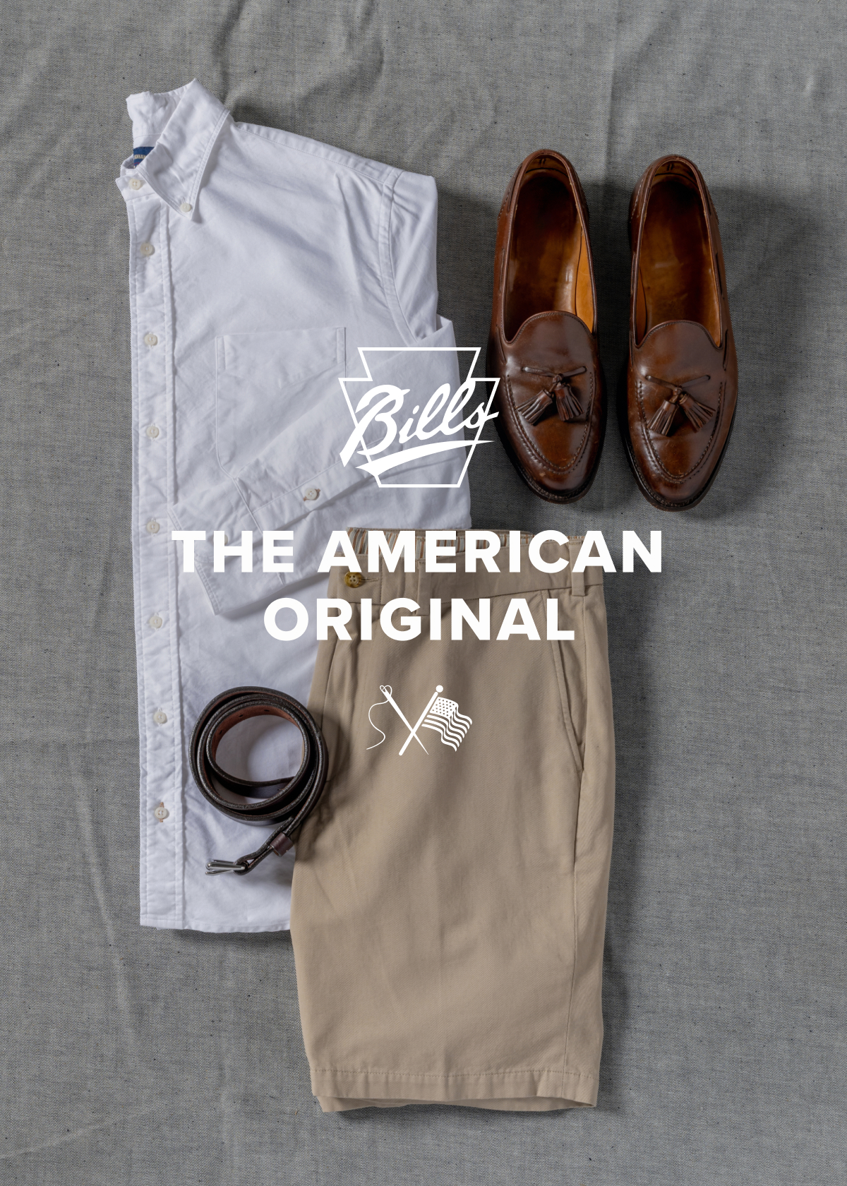 A timless Bills Khakis outfit consisting of shorts, belt, and standard fit shirt lays on a grey fabric surface