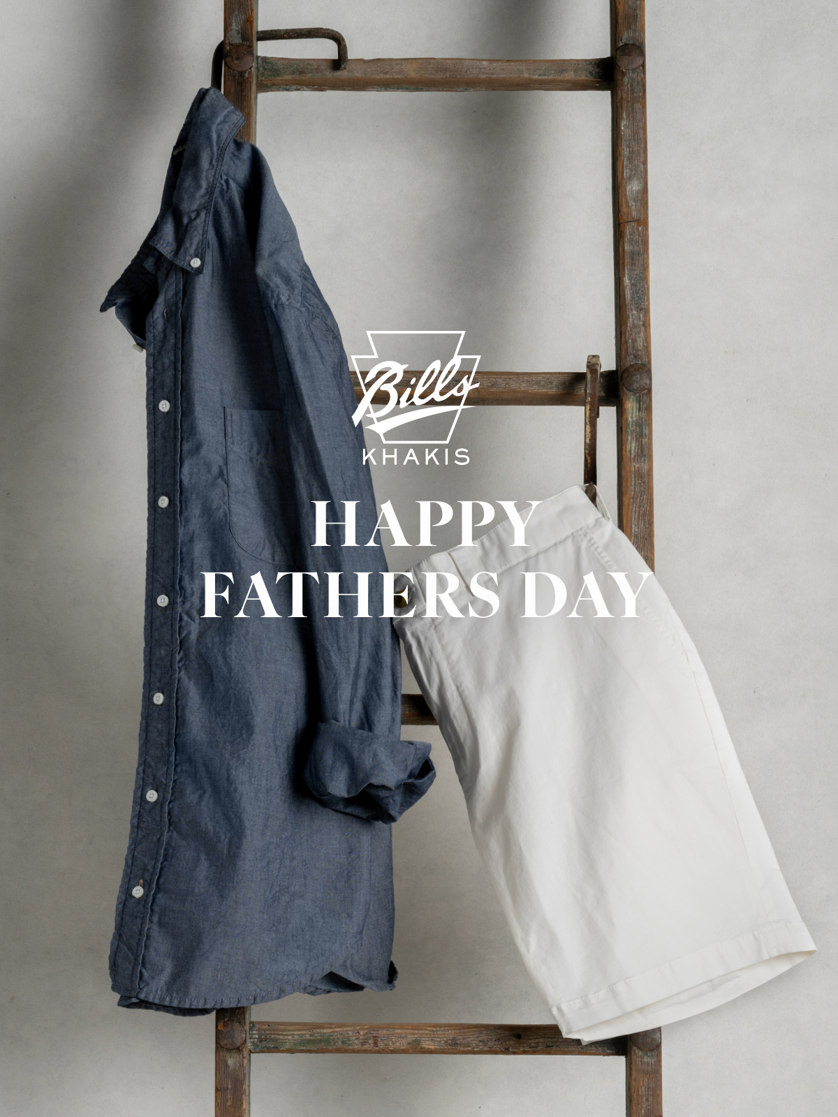 A Bills Khakis Standard fit shirt and shorts hang from a vintage wooden ladder. The Bills Khakis logo overlays the photo with text that reads Happy Fathers Day