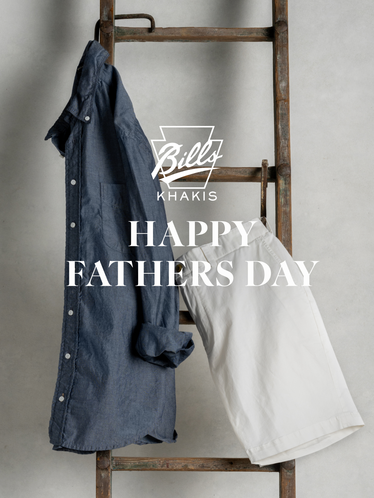 A Bills Khakis Standard fit shirt and shorts hang from a vintage wooden ladder. The Bills Khakis logo overlays the photo with text that reads Happy Fathers Day