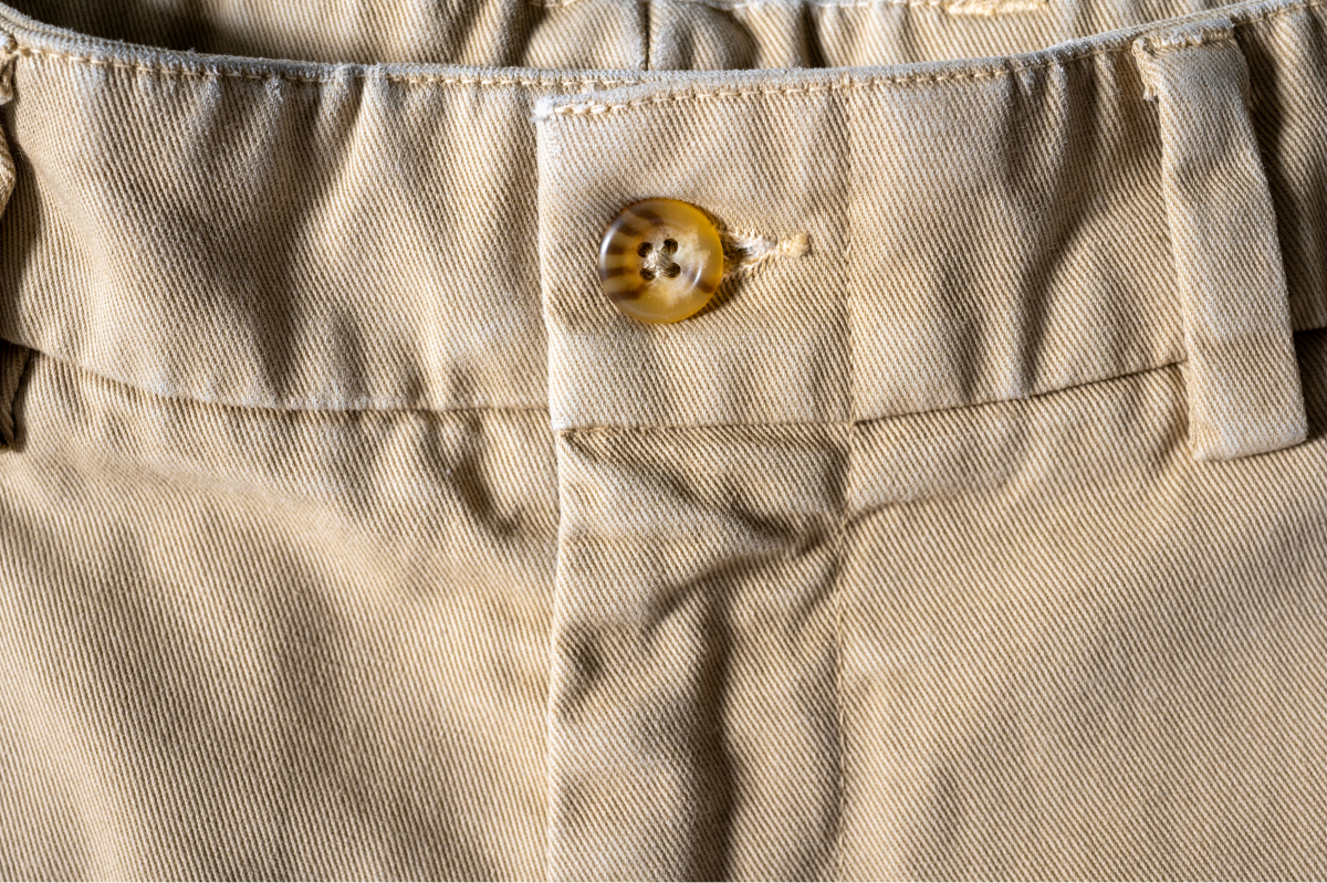 A closeup of a the button and belt seam of a pair of kahki colored Bills Khakis Heritage wash pants