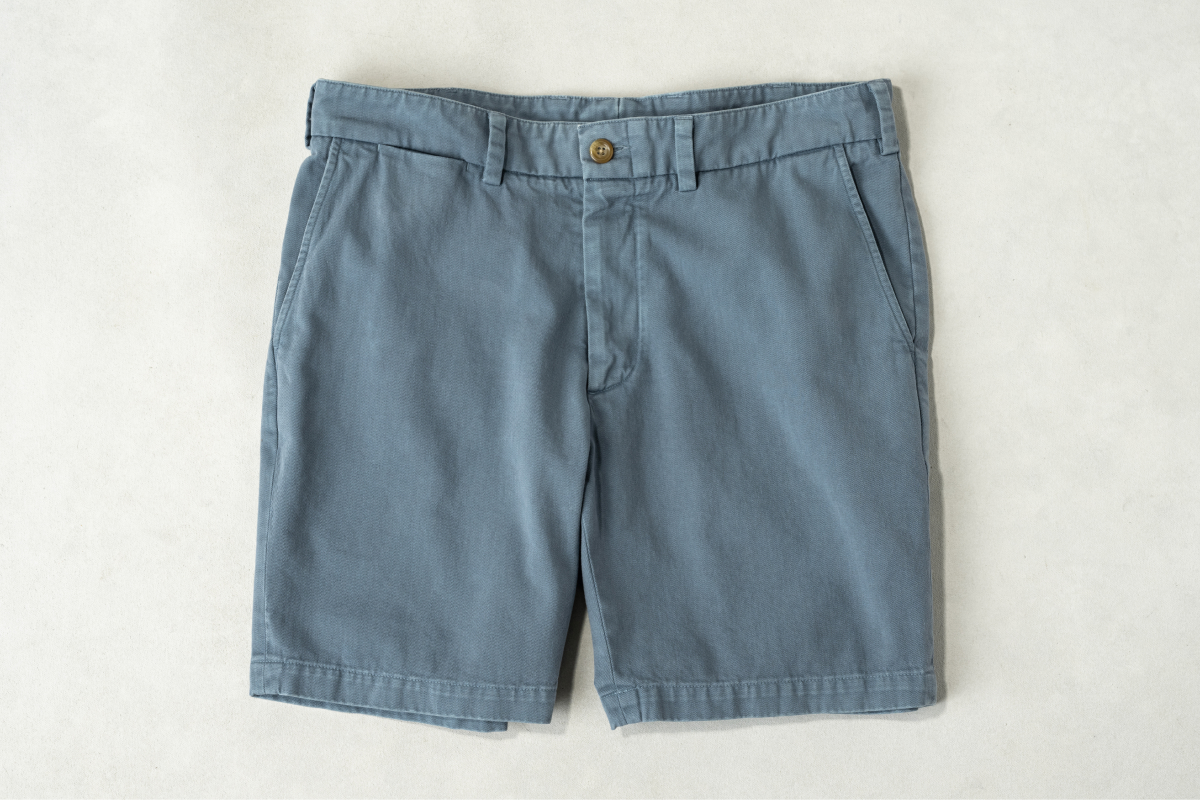 A dusty blue pair of Bills Khakis Heritage Wash twill shorts lay on a light backdrop