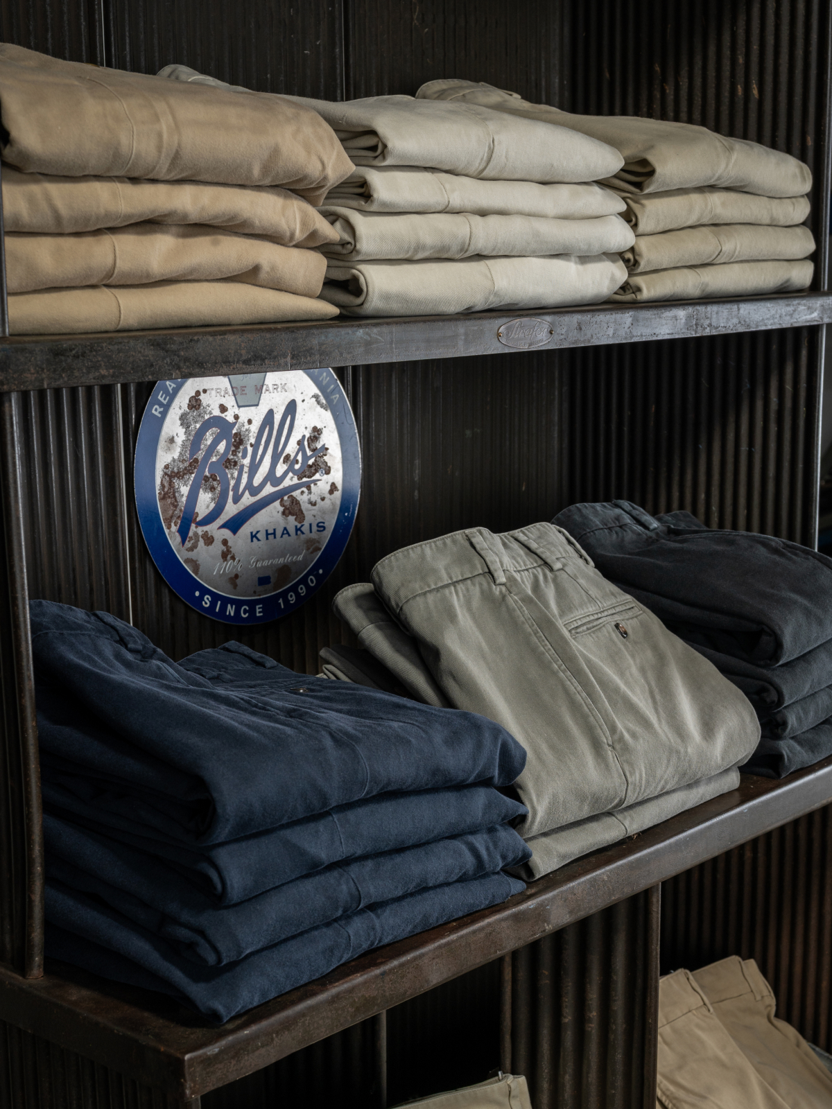 An array of Heritage wash pants sit folded in a vintage steel shelving unit